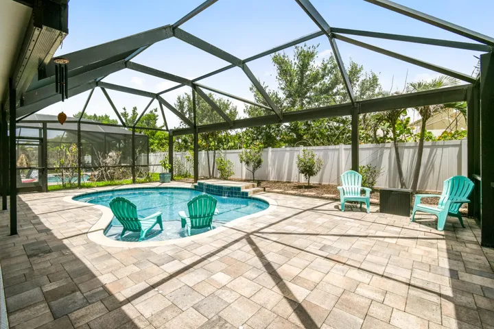 Screened-in outdoor pool area featuring a freeform saltwater heated swimming pool with layout pad and a waterfall feature, surrounded by paver decking