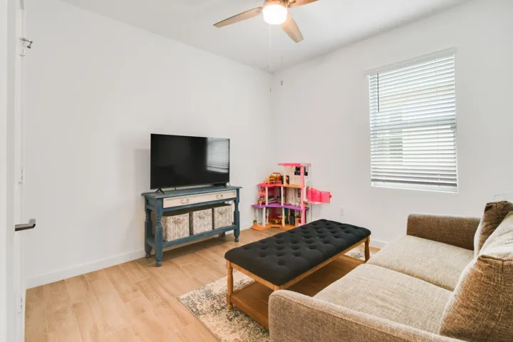 Room featuring wood-finish flooring, a ceiling fan with integrated lighting, and a window with blinds