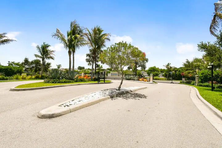 Paved entrance road with a central landscaped median leads to security gate call box.