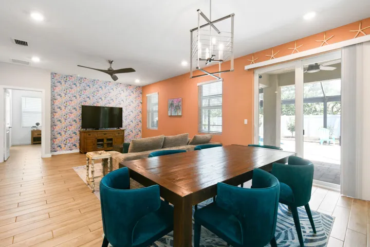 Spacious dining area featuring a dark wood-finish table, a modern rectangular chandelier, and large sliding glass doors leading to spacious pool patio and lanai