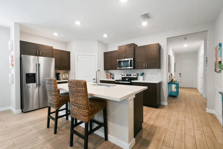 Modern kitchen featuring a central island with an integrated sink, stainless steel appliances, dark wood-finish cabinetry, a white countertop, and wood-finish flooring