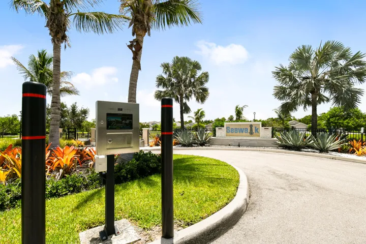 Gated community entrance featuring a stone monument "SeaWalk" entry with tropical landscaping, and mature palm trees