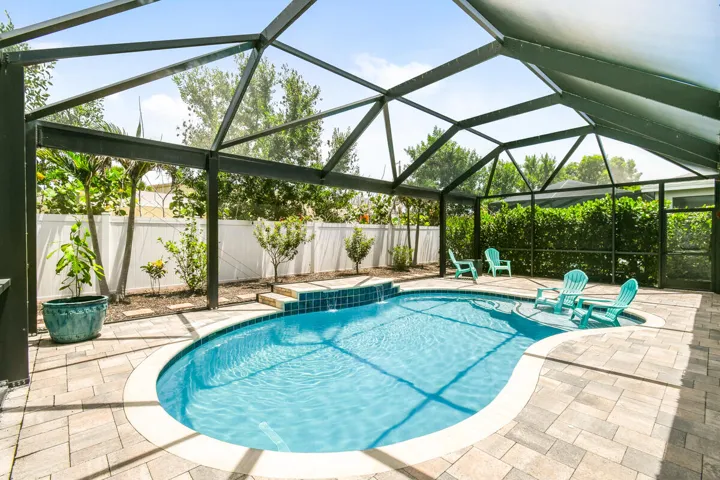Screened-in pool featuring a paved patio surround and a tile-finished water feature