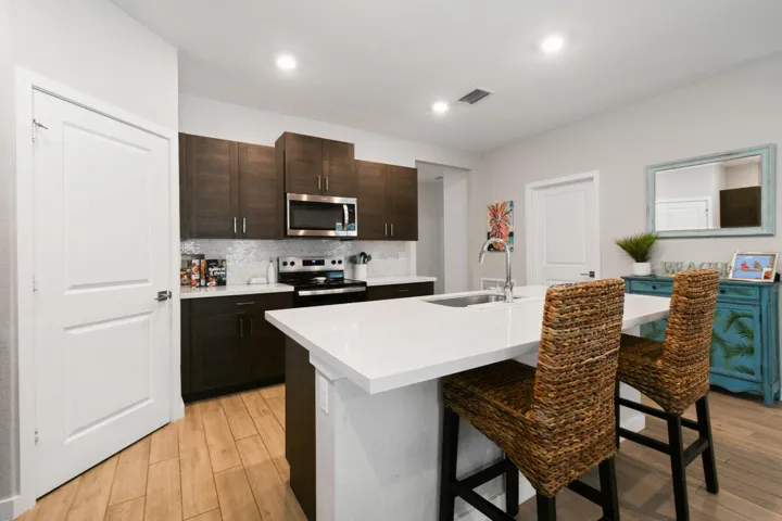Modern kitchen featuring dark wood-finish cabinetry, stainless steel appliances, a white tile backsplash, and a large central island with a white countertop and integrated sink