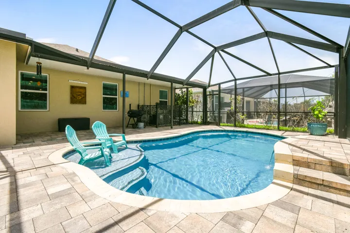 Screened-in pool area featuring a freeform swimming pool with integrated steps, paver decking, and a covered patio