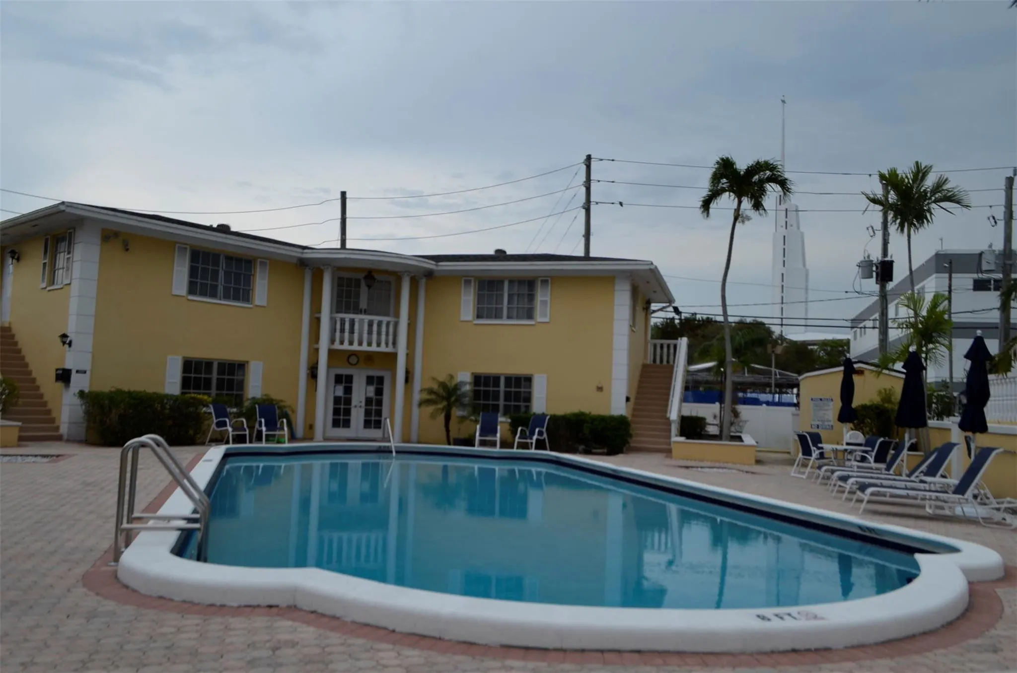 Inviting outdoor pool area featuring a freeform pool with integrated steps, surrounding brick paver patio, and low-rise residential building with a central balcony