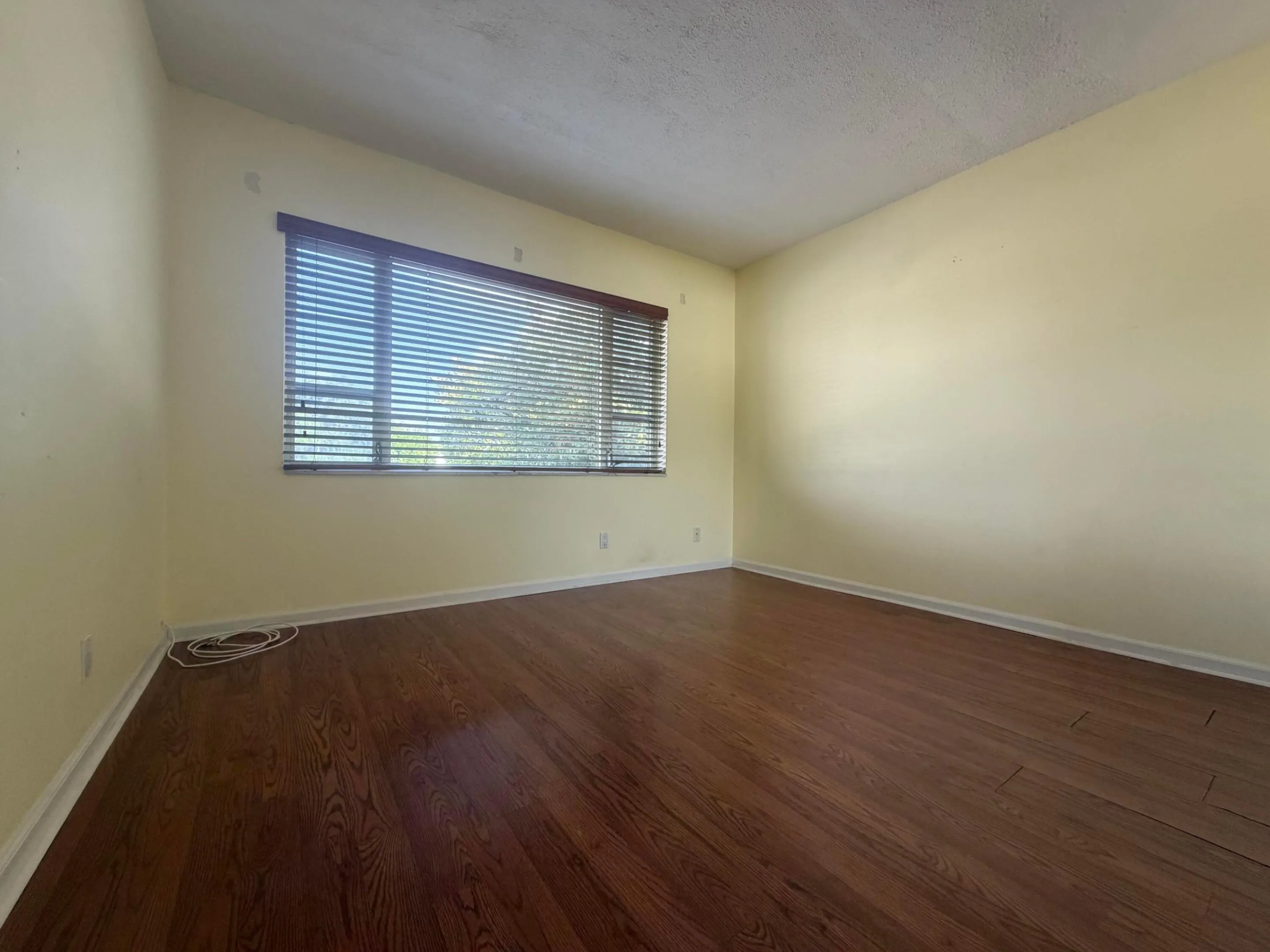 Bedroom view featuring wood-finish flooring and light-toned walls, window with blinds.