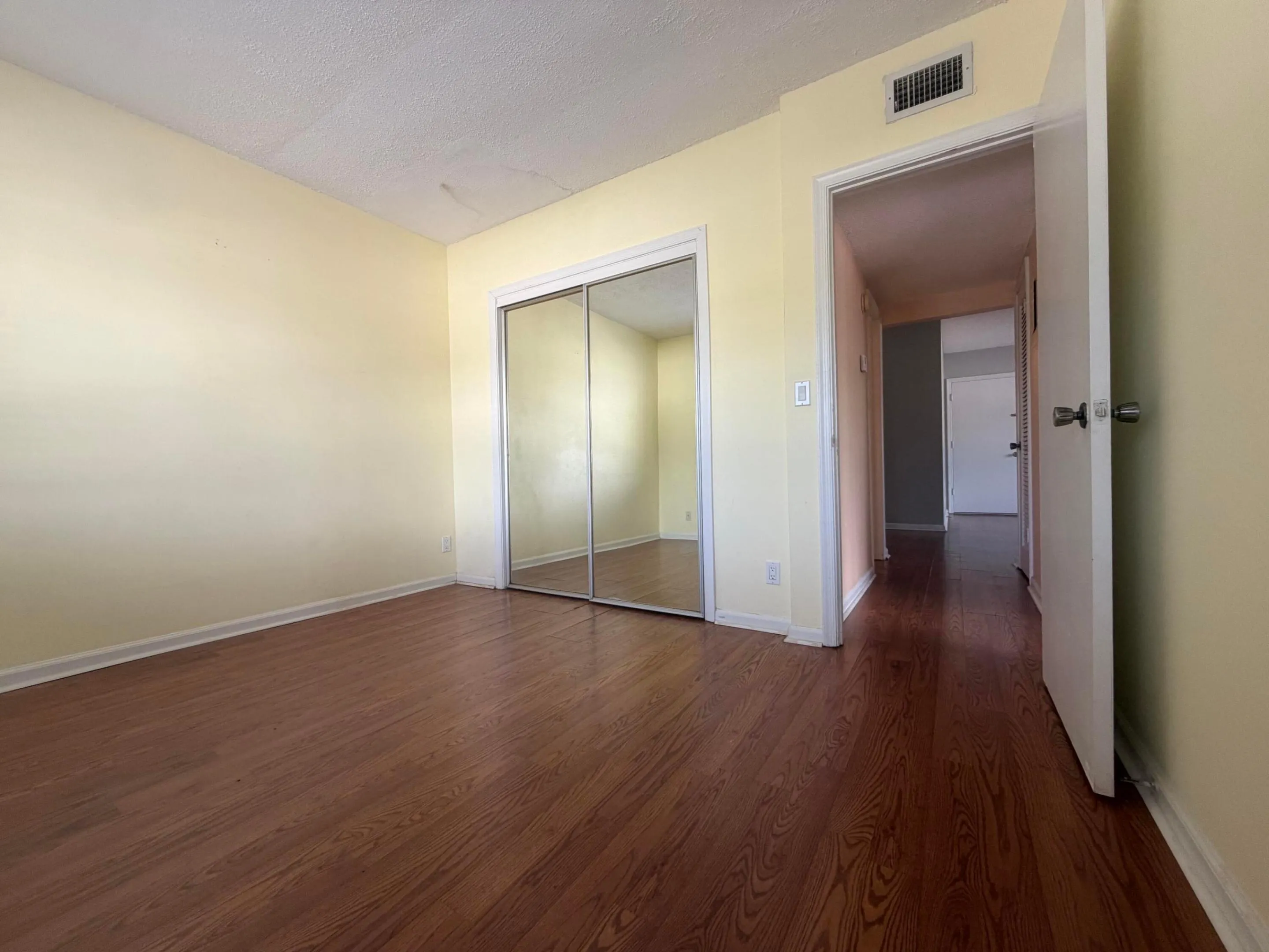 Bedroom featuring wood-finish flooring and light-toned walls, mirroed closet doors.