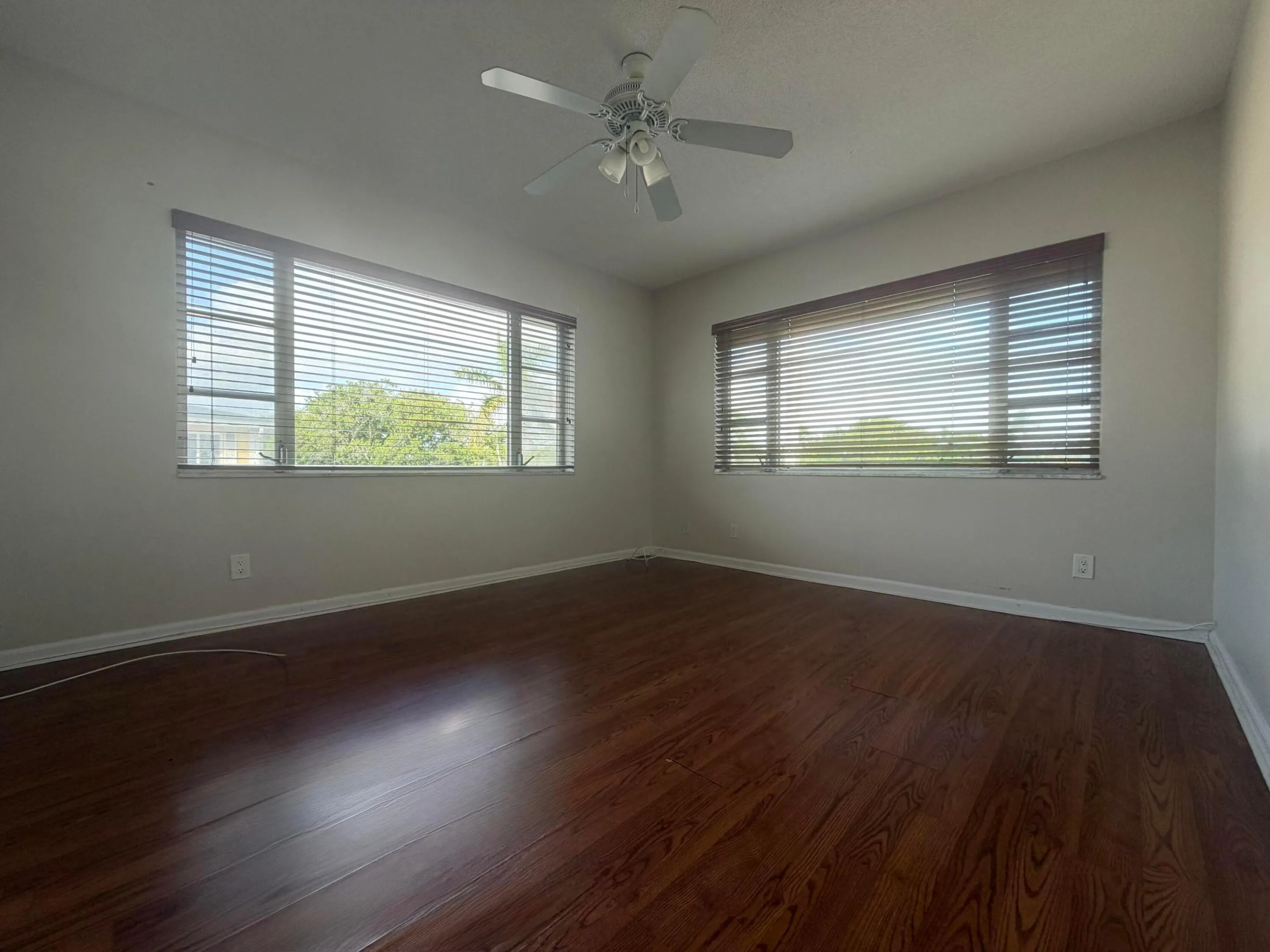 Bedroom featuring wood-finish laminate flooring and light-toned walls, 2 windows with blinds.