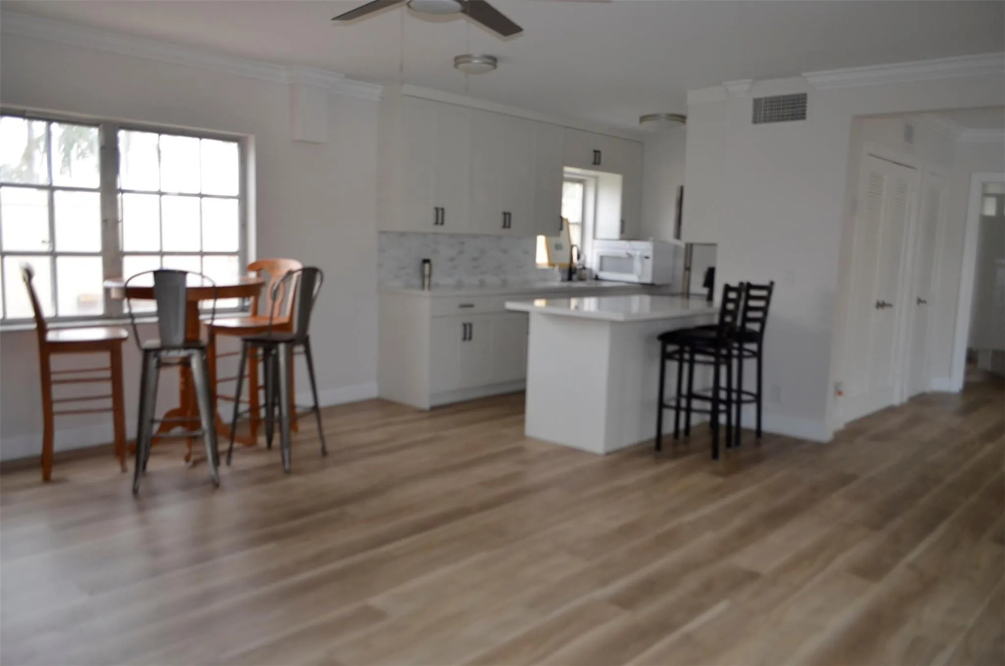 Recreation area with Open-concept kitchen and living area featuring wood-finish flooring, white cabinetry, a kitchen island with a light-toned countertop, and a patterned backsplash
