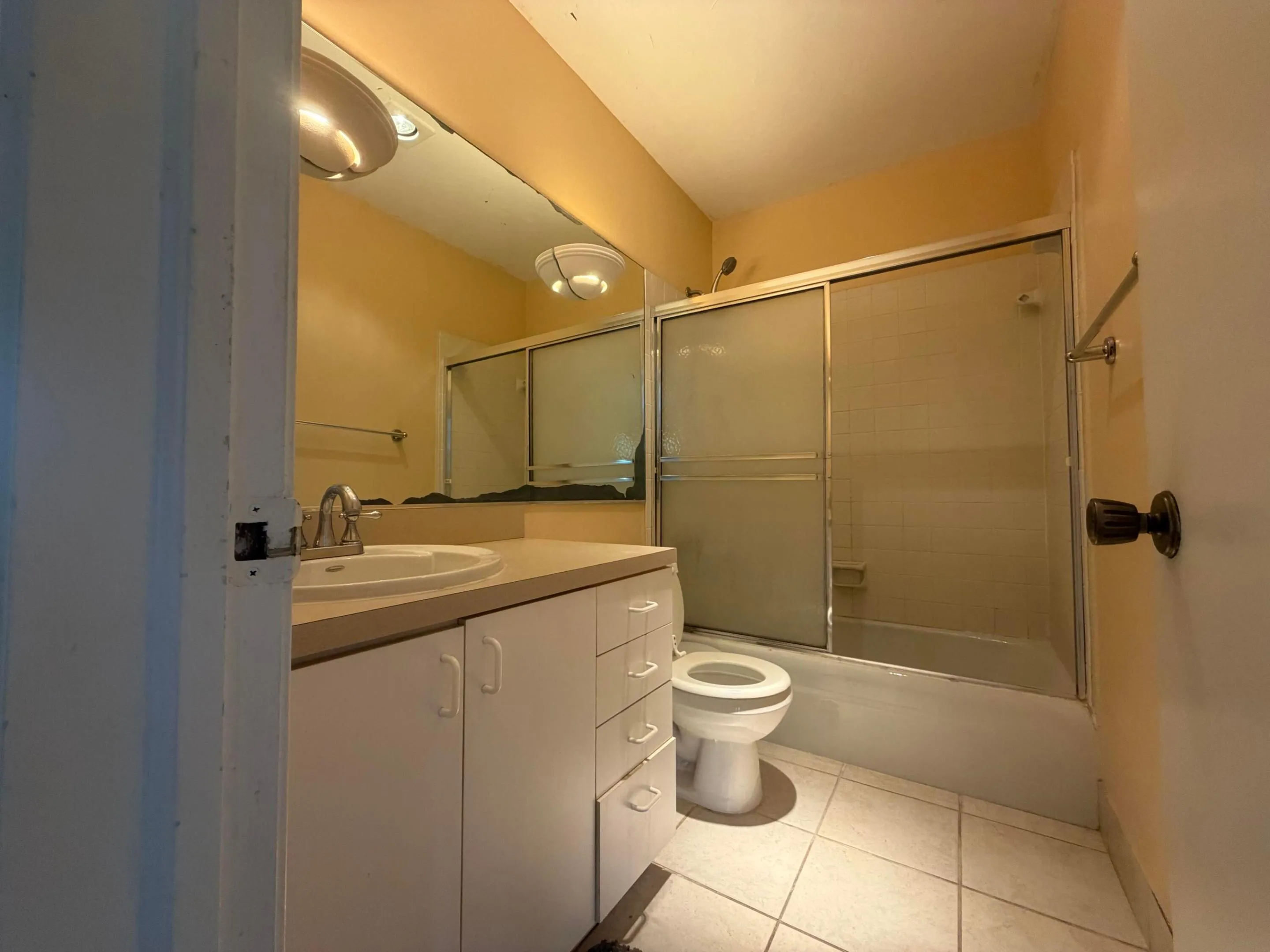 Bathroom featuring a built-in vanity with integrated sink, a shower-tub combination with glass shower doors, a wall-mounted towel bar, and ceramic tile flooring.