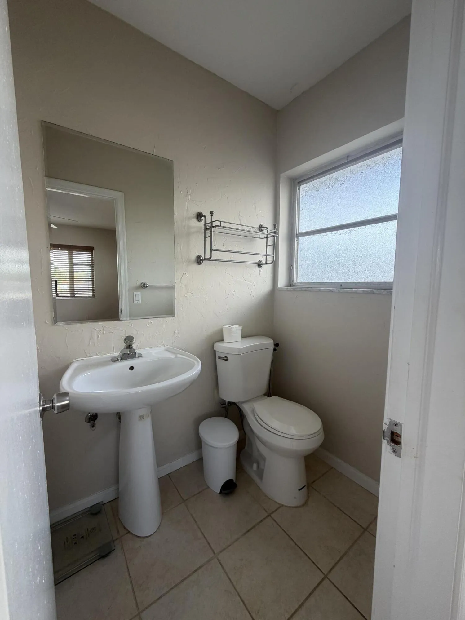 Pedestal sink with chrome faucet, wall-mounted mirror, and tile flooring.