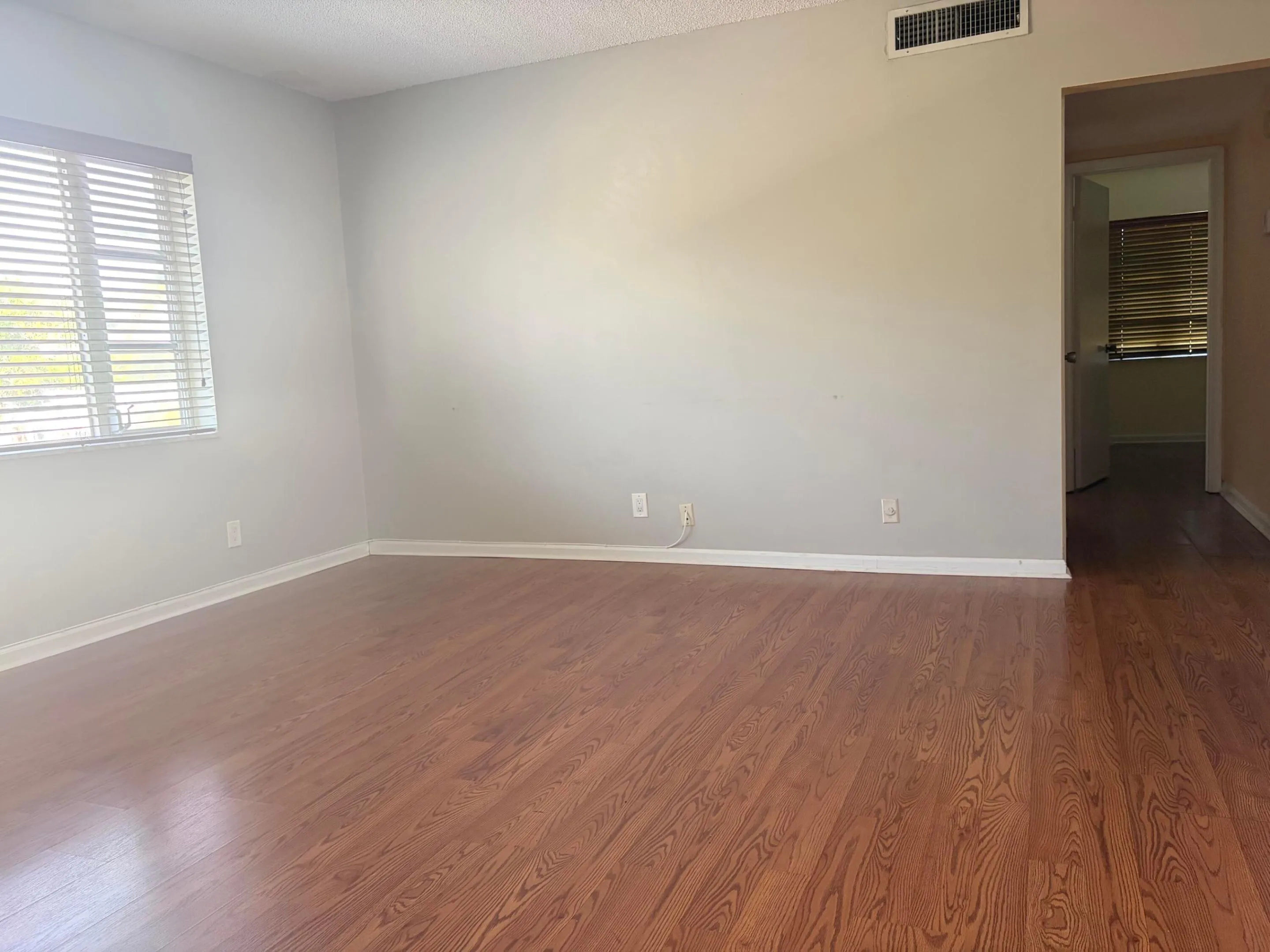 Spacious living area featuring laminate flooring, a large window with blinds, and neutral wall tones.