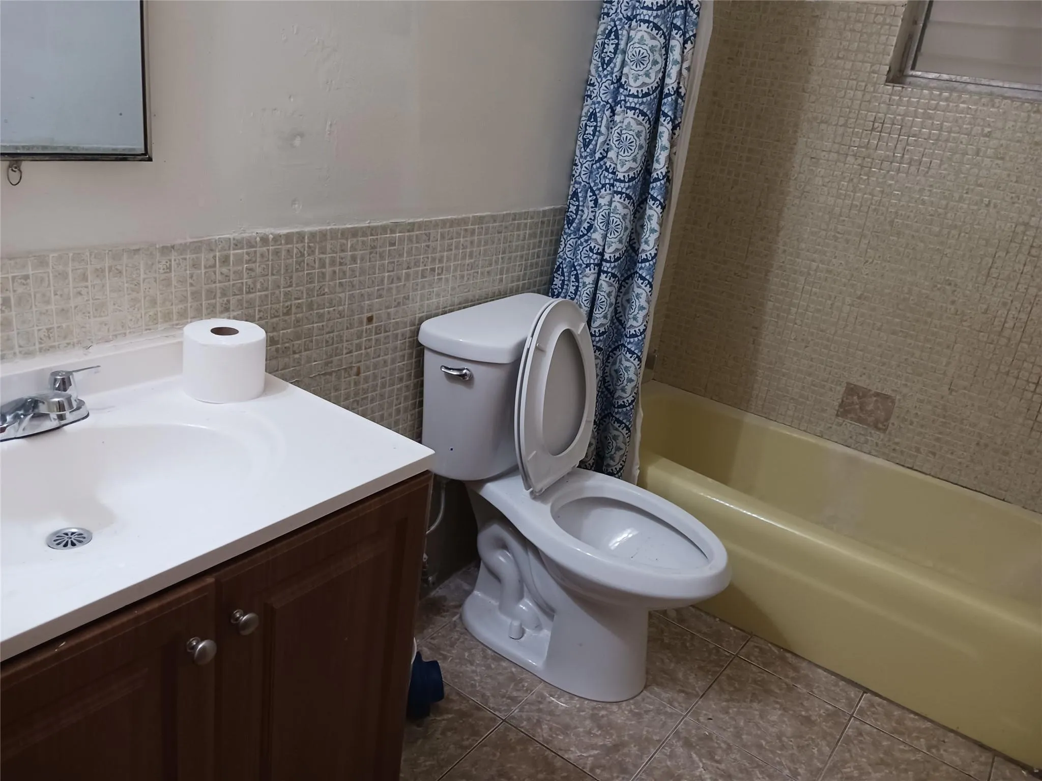 Bathroom featuring a white toilet, a vanity with a white countertop and brown cabinetry, and a bathtub with a shower curtain