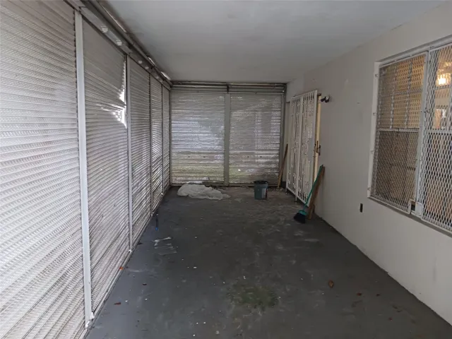 Enclosed patio featuring a concrete floor, security bars, and a white painted wall