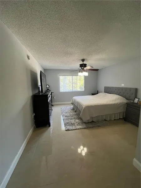 Spacious room featuring light-toned tile flooring, a window with vertical blinds, and a ceiling fan with integrated lighting