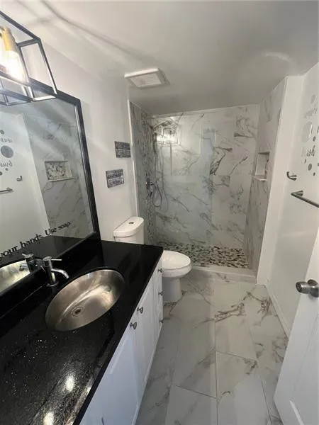 Contemporary bathroom featuring a white vanity with black countertop, a stainless steel undermount sink, a walk-in shower with stone tile flooring, and large format marble-look wall and floor tiles