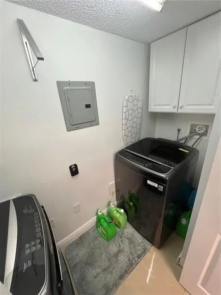 Dedicated laundry space featuring white upper cabinetry, light-toned flooring, and a compact wall-mounted drying rack
