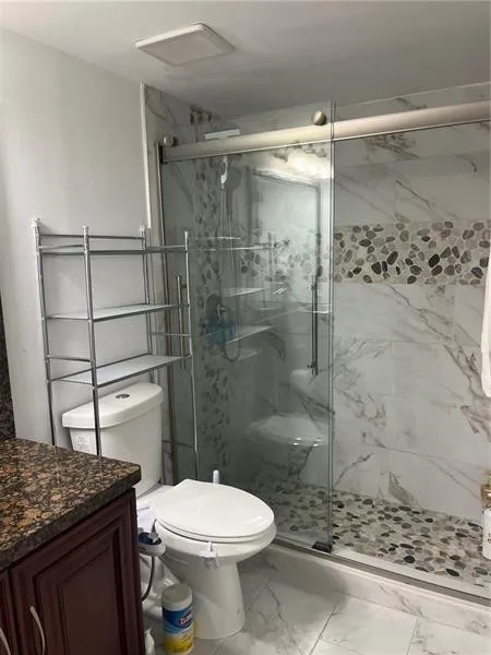 Full bathroom featuring a glass-enclosed shower with sliding door, pebble tile shower floor, large format white marble-look wall tiles, and a coordinated pebble tile accent band