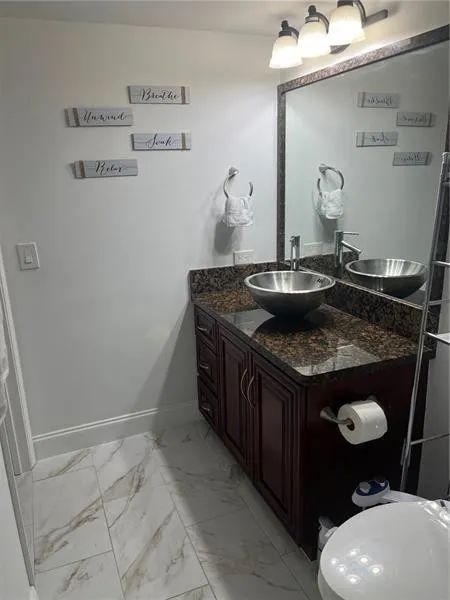 Bathroom vanity featuring a vessel sink with a single-handle faucet, granite countertop, dark wood-finish cabinetry, and a framed mirror
