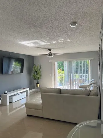 Spacious living area featuring polished tile flooring, a ceiling fan, and a built-in media console