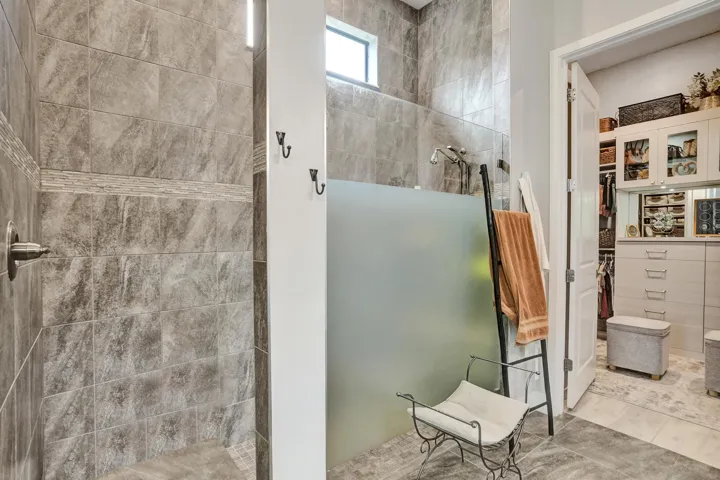 Walk-in shower featuring large floor to ceiling tile, a tiled shower bench, with semi-opaque glass
