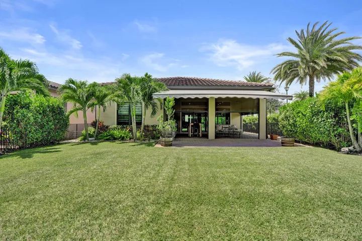 Expansive rear yard featuring a manicured lawn, lush perimeter landscaping, and a covered patio with a motorized awning