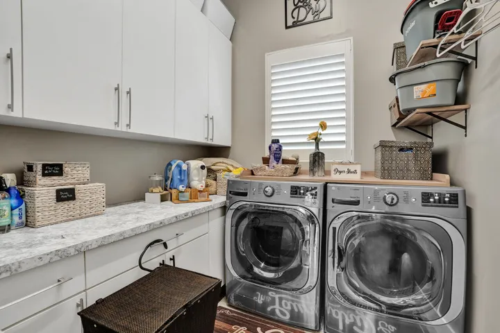 Functional laundry room featuring a pair of front-loading washer & dryer, ample white cabinetry, and a sink