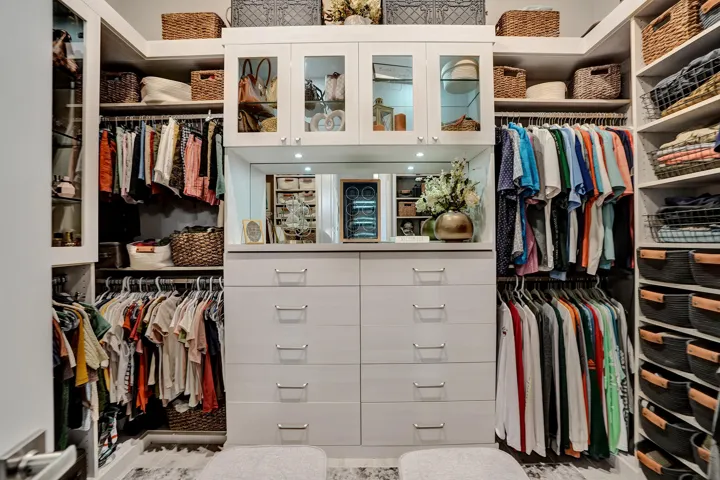 Custom closet system featuring a central dresser unit, mirrored accents, and integrated upper cabinetry with glass-front doors