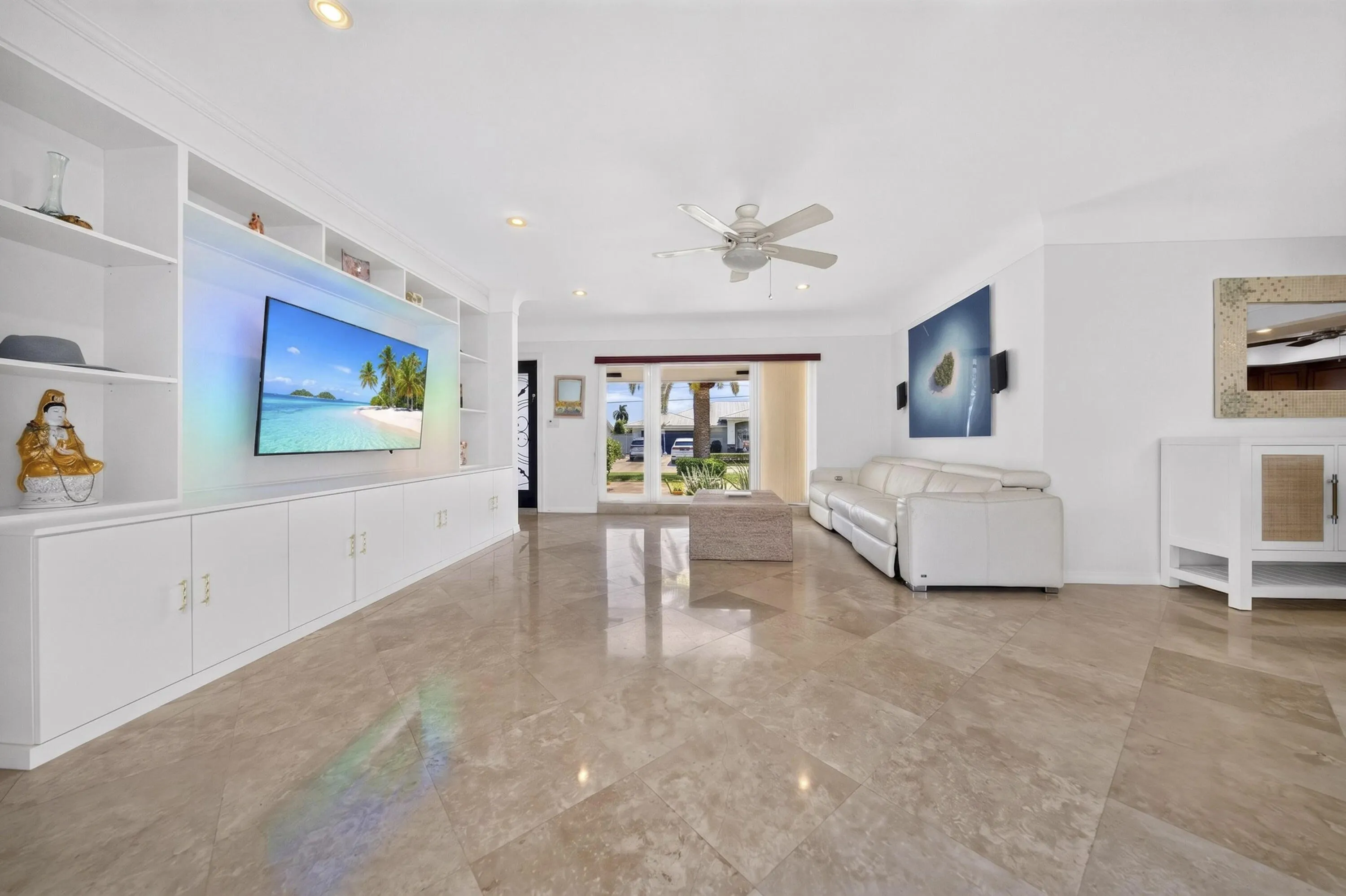 Spacious living area featuring polished Travertine marble flooring, a built-in entertainment center with open shelving and lower cabinetry, a ceiling fan, recessed lighting, and a wide entryway with double glass doors
