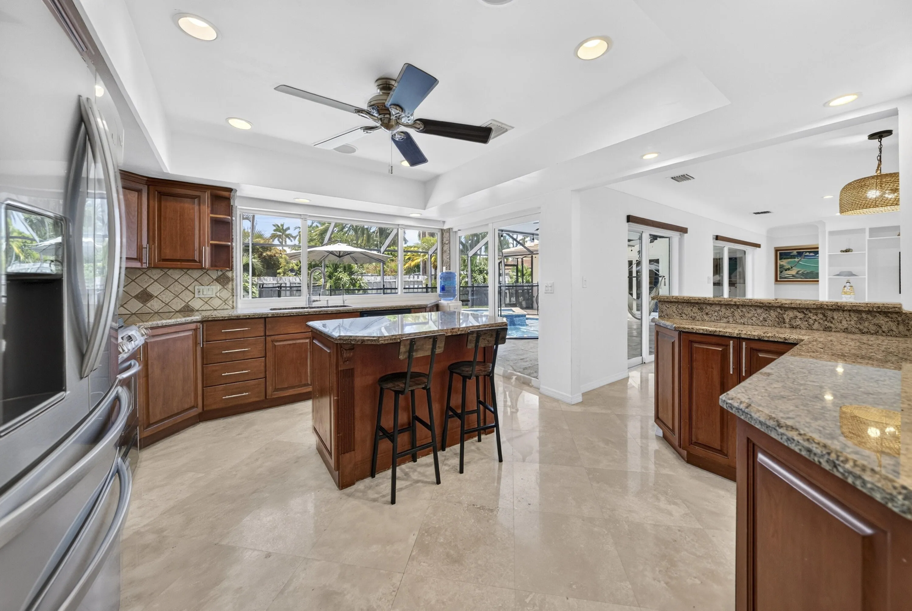 Spacious kitchen featuring warm wood cabinetry, stone countertops, a tiled backsplash, recessed lighting, and a central island with seating