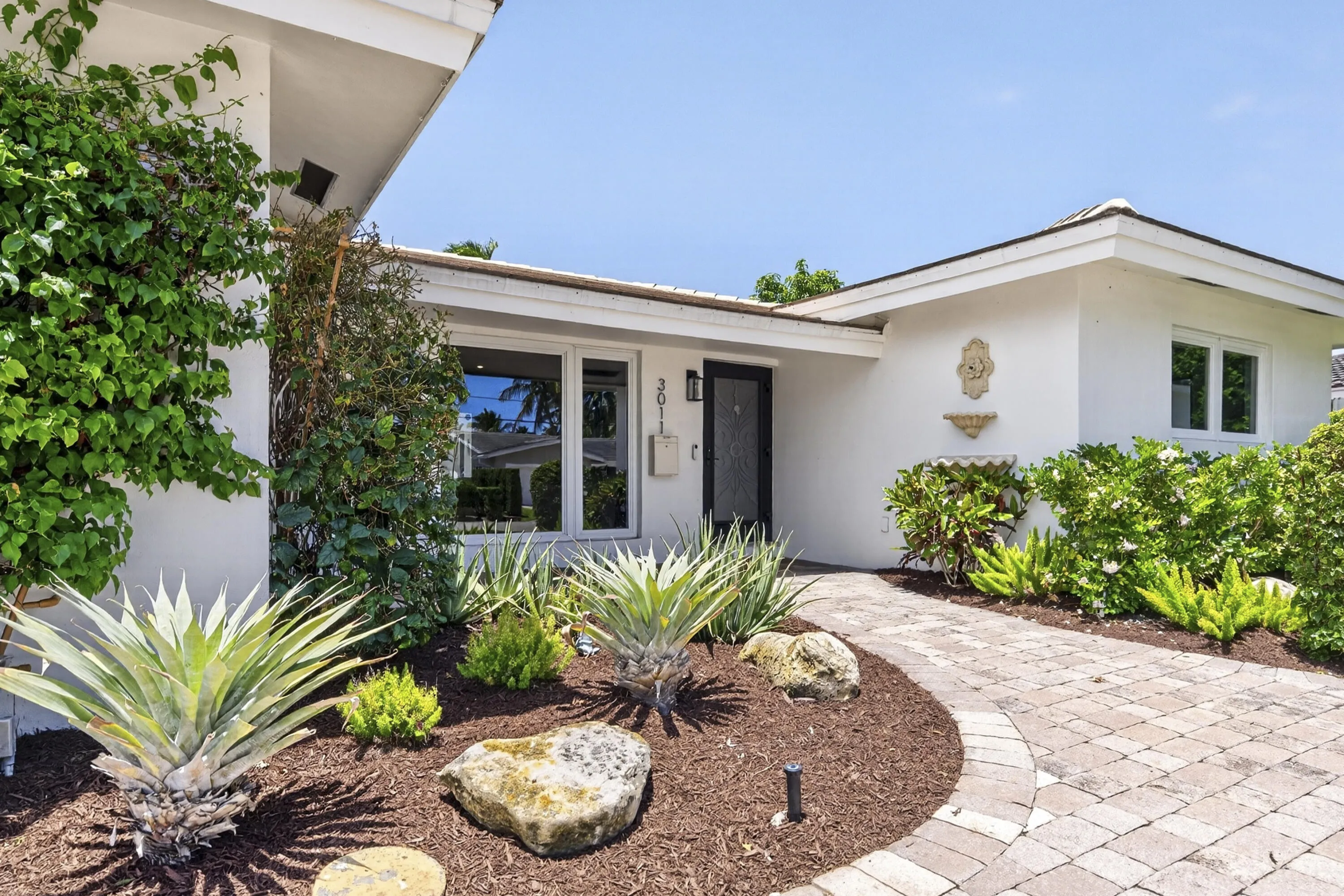 White stucco exterior with a dark entry door, framed by a paver walkway