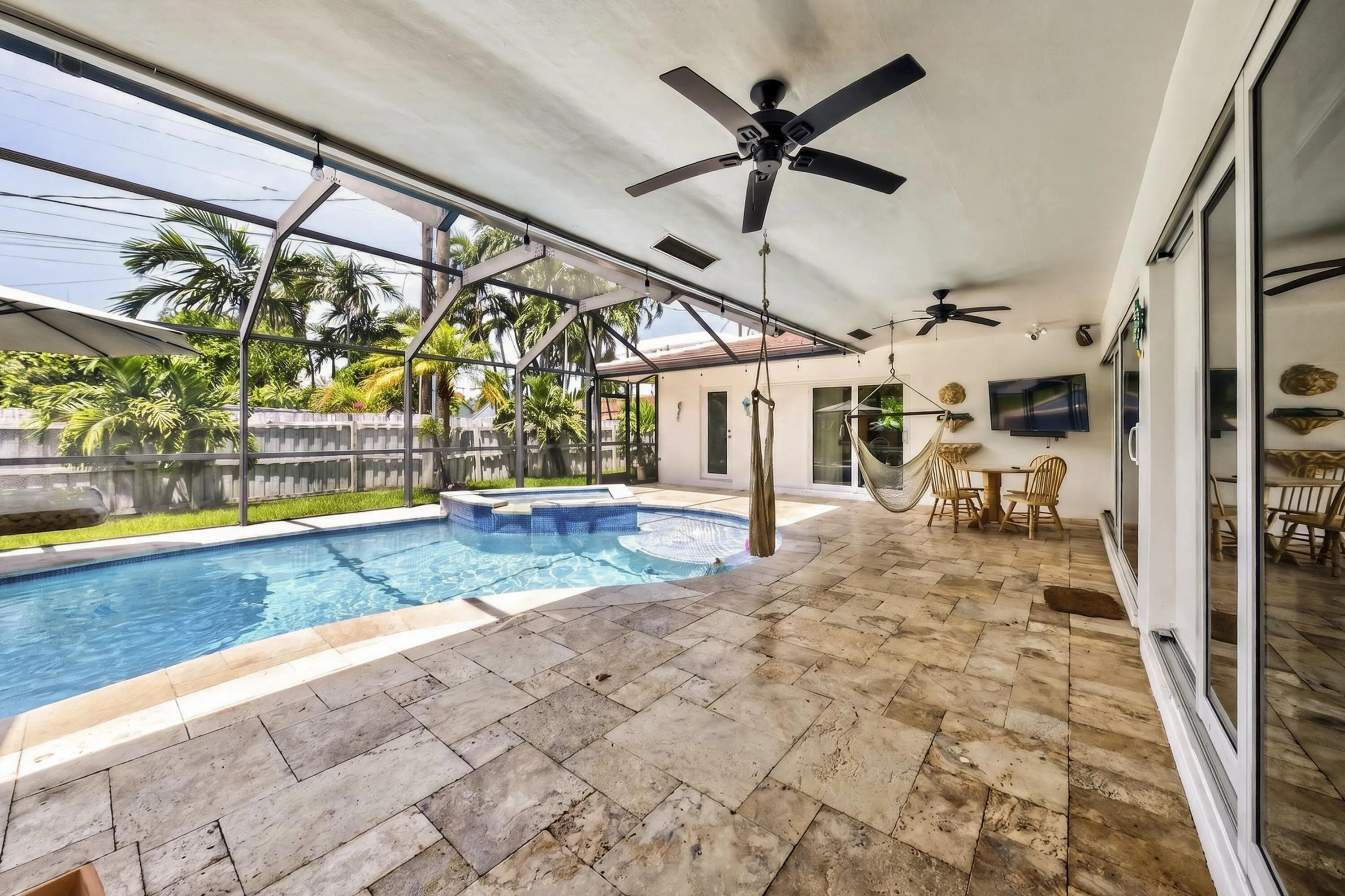 Screened patio featuring a swimming pool with attached spa, extensive stone-finish flooring, and multiple ceiling fans