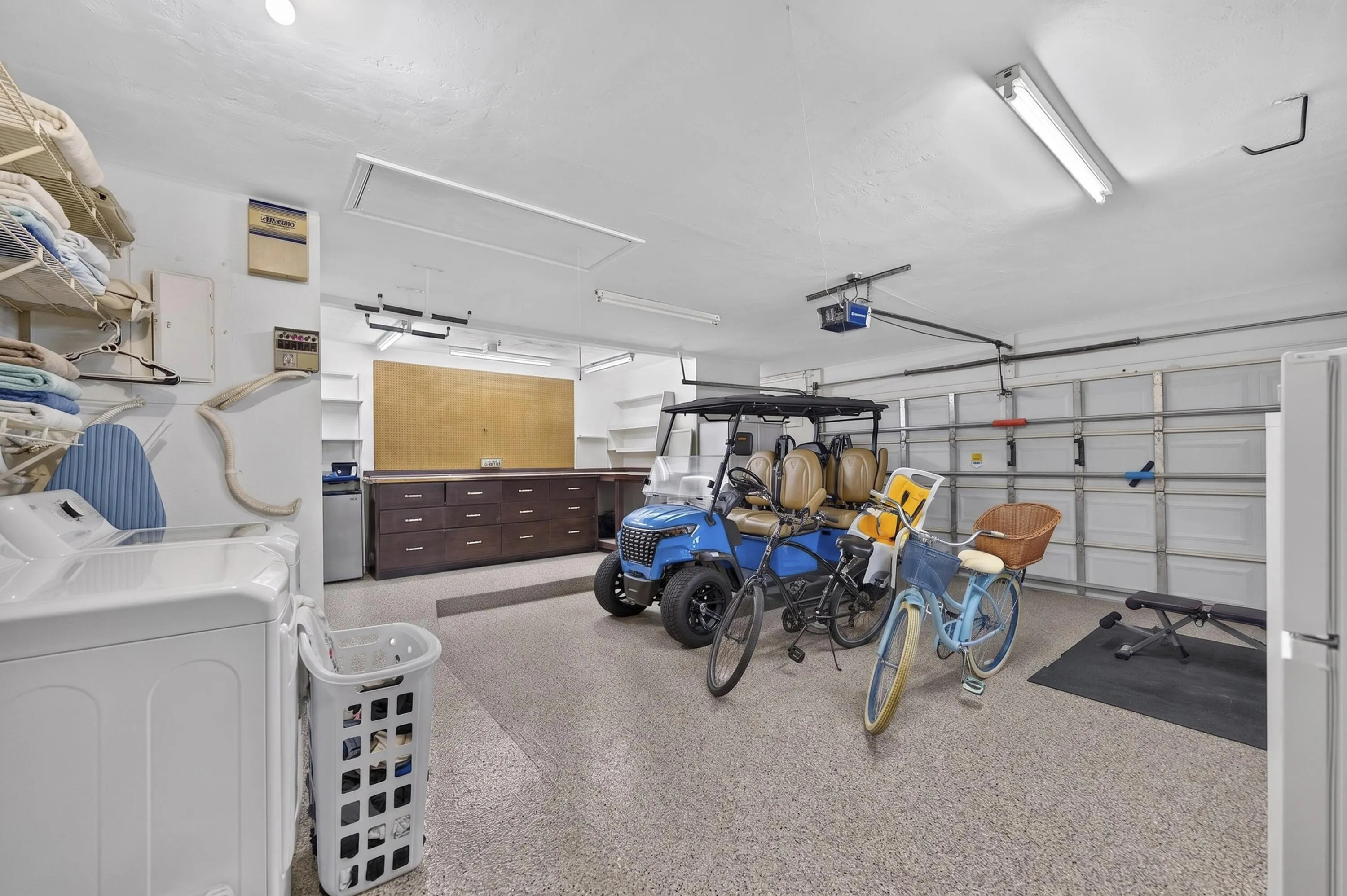 Spacious garage featuring a durable speckled epoxy floor, large alcove with built-in workbench, storage, fluorescent overhead lighting, and white paneled garage doors