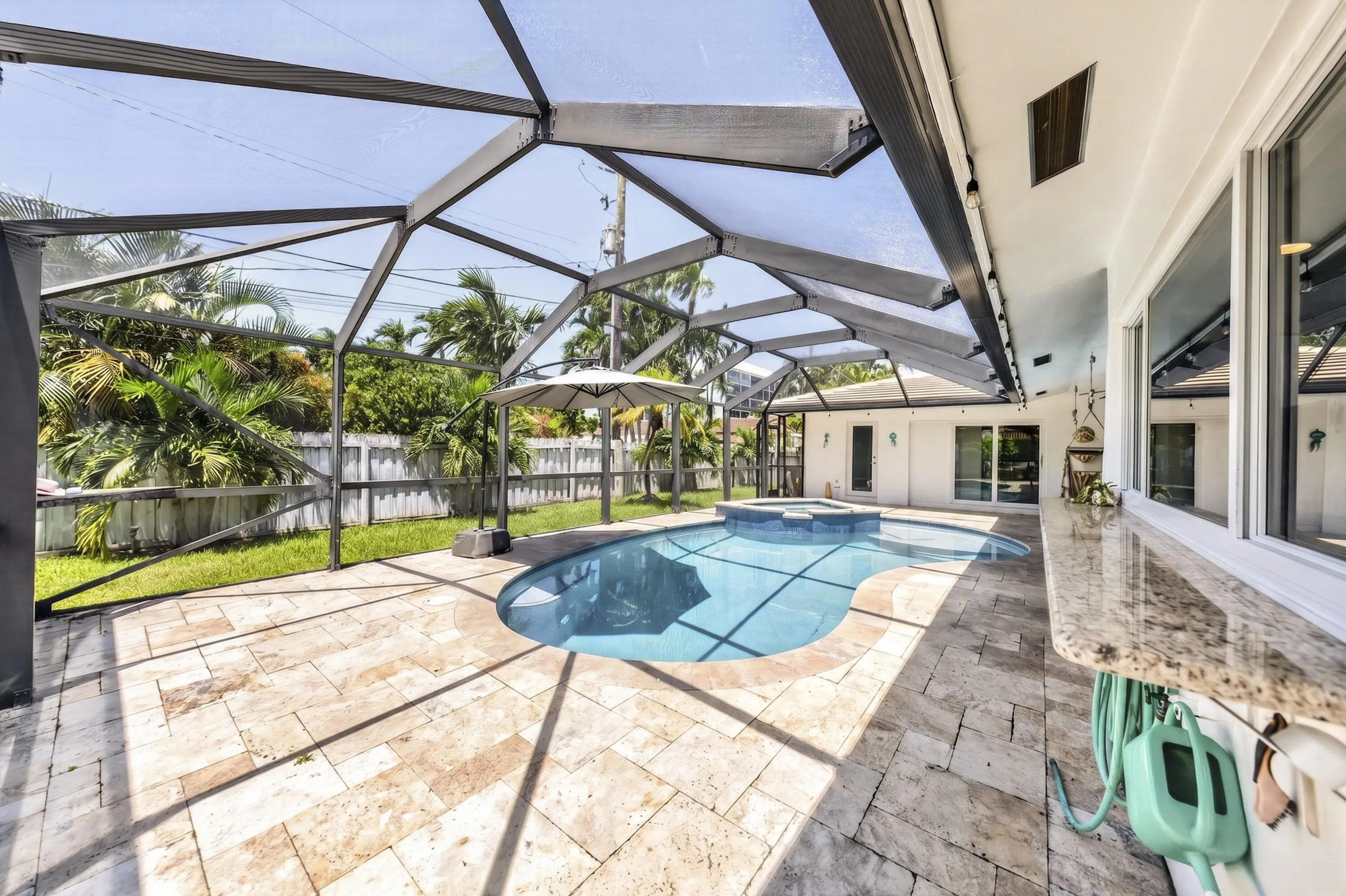 Screened outdoor living area featuring a freeform swimming pool with integrated spa, extensive stone paver decking, and a built-in outdoor bar with a stone countertop