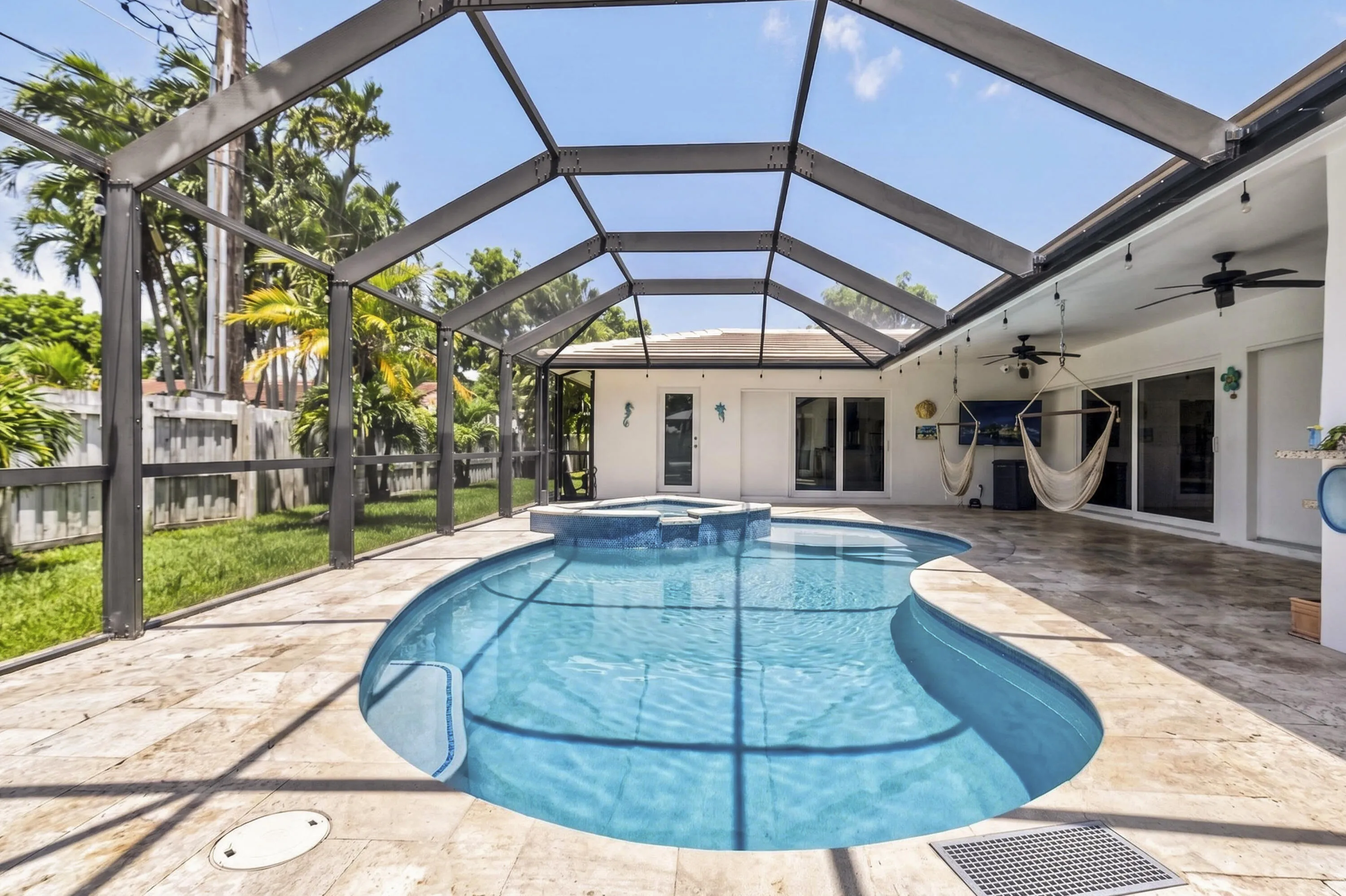 Screened-in outdoor area featuring a freeform pool with an integrated spa, extensive stone paver decking, and a covered patio with ceiling fans and recessed lighting