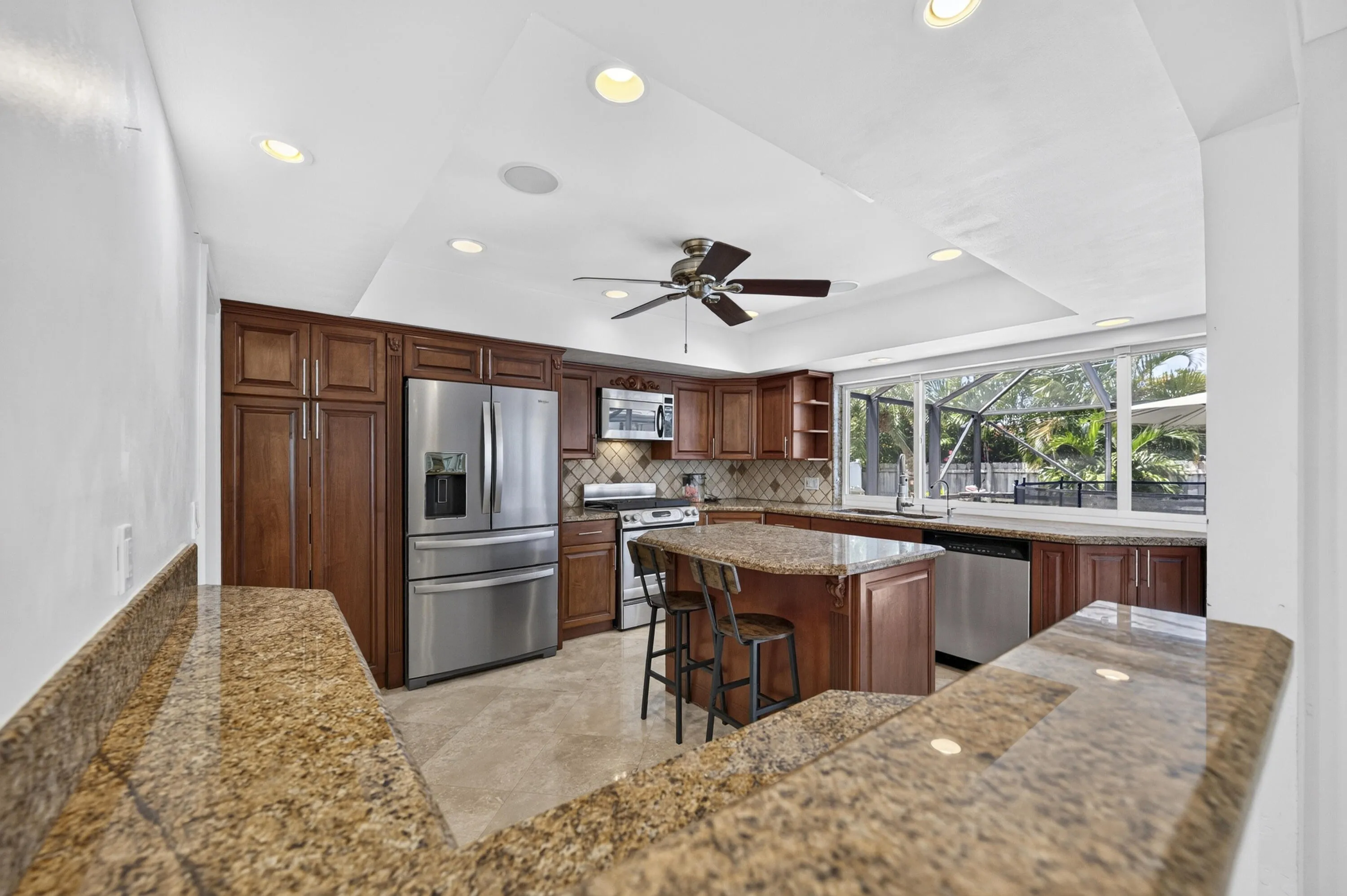 Kitchen featuring a large island with seating, extensive granite countertops, stainless steel appliances, dark wood cabinetry, and recessed lighting