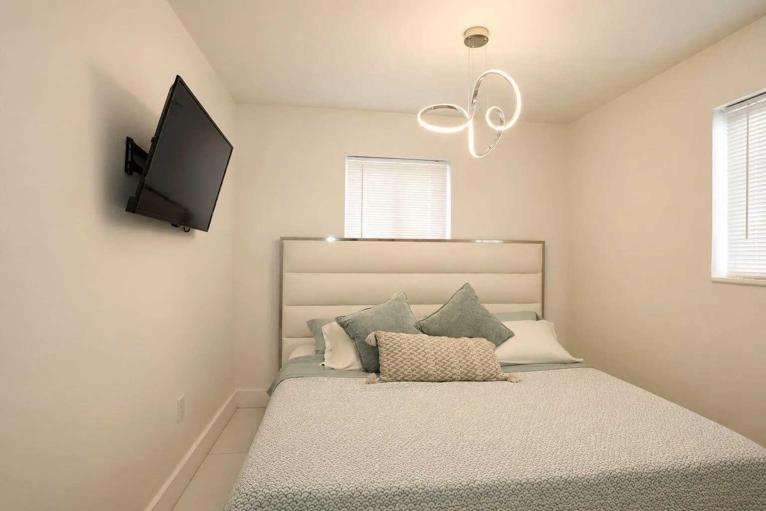 Room featuring light-toned walls, a decorative ceiling fixture, and two windows with blinds
