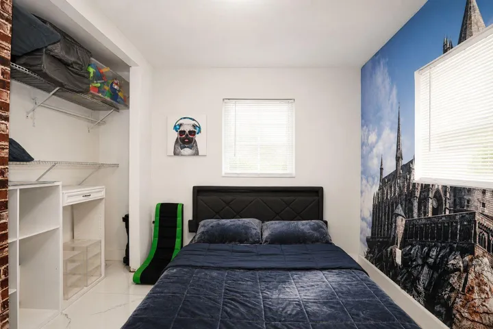 Bedroom featuring a window with horizontal blinds, a decorative wall mural, and light-colored flooring