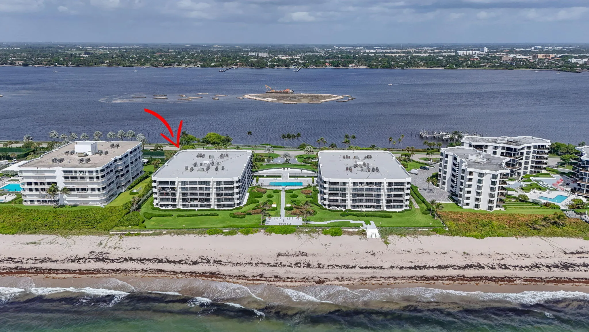 Beachfront residential building featuring multiple private balconies, landscaped grounds, a community pool, and direct beach access