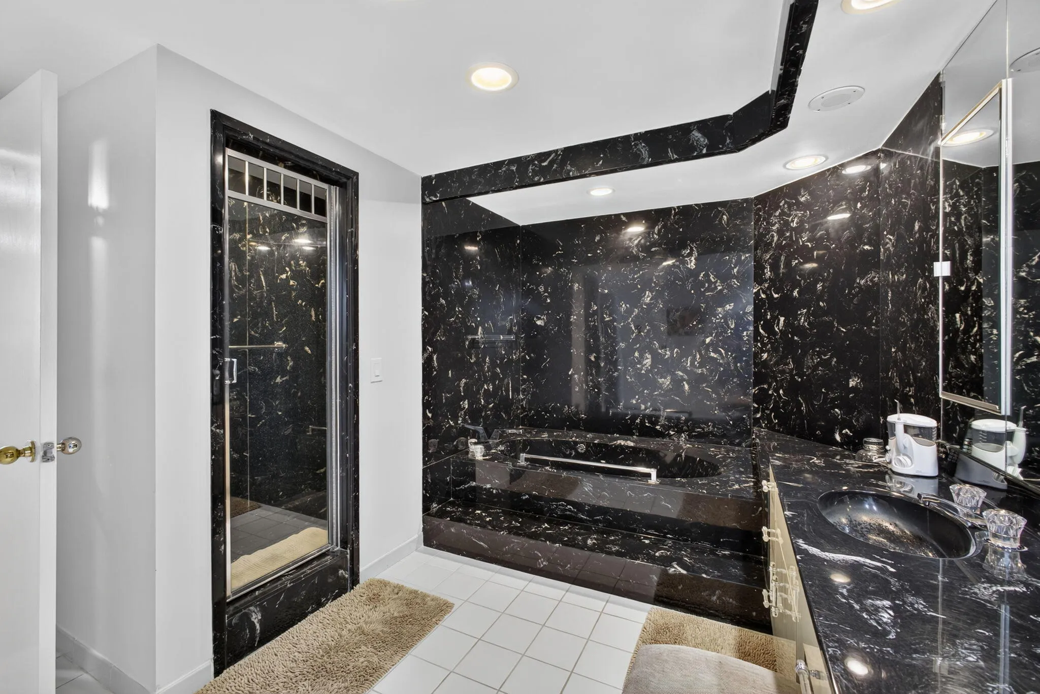 Bathroom featuring black patterned wall panels, a built-in tub with matching surround, a glass-enclosed shower, a vanity with a black integrated sink, and white floor tiles