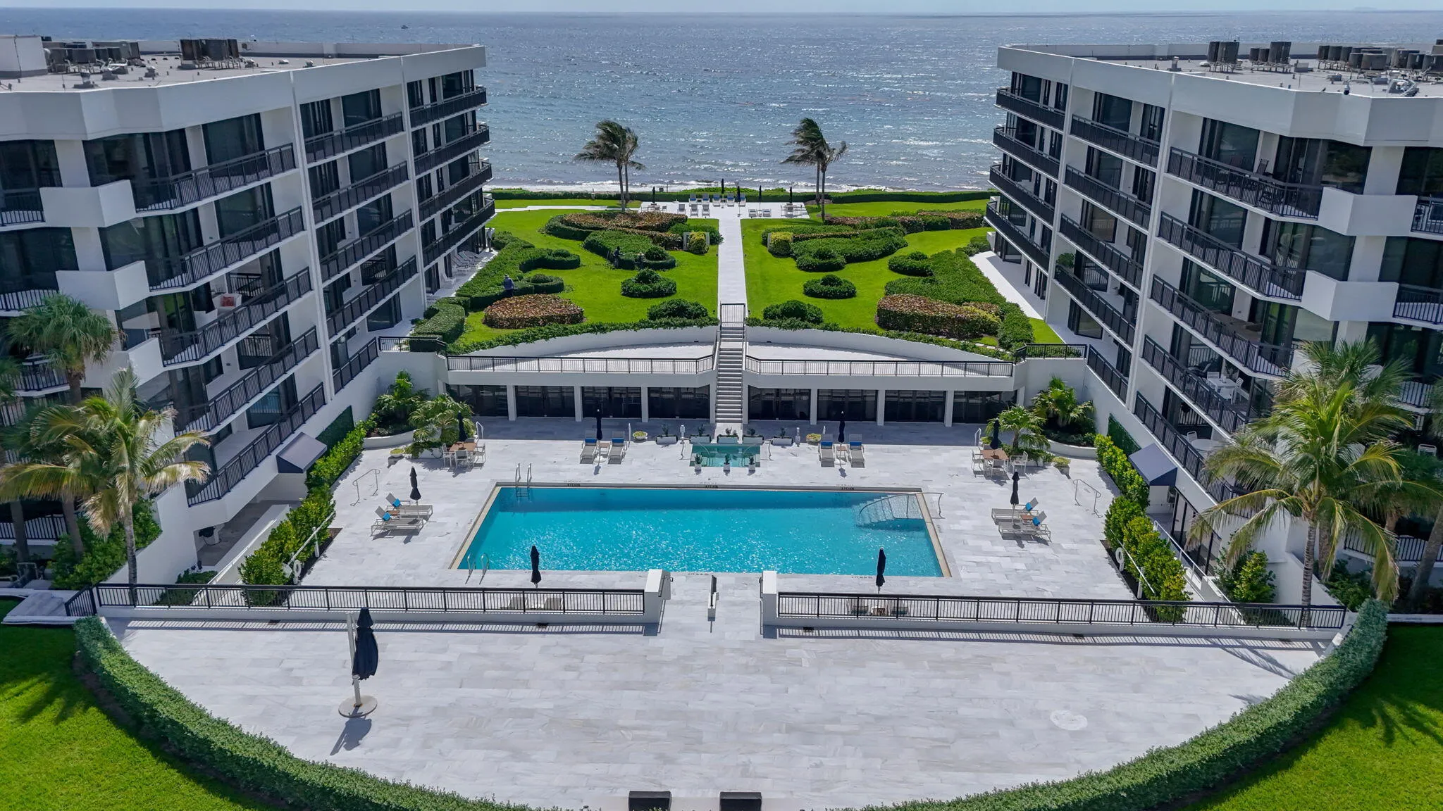 Resort-style complex featuring two multi-story buildings, a central swimming pool, and landscaped green spaces