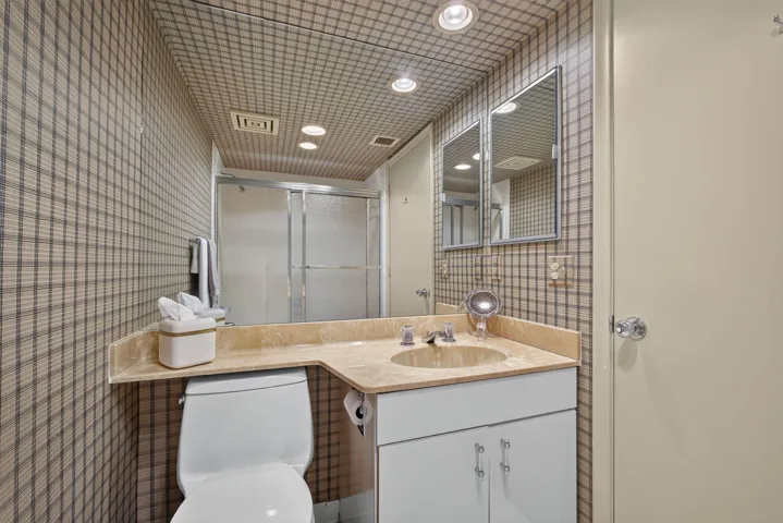 Bathroom featuring patterned wallpaper, a built-in vanity with an integrated sink and stone countertop, recessed lighting, and a shower with frosted glass enclosure