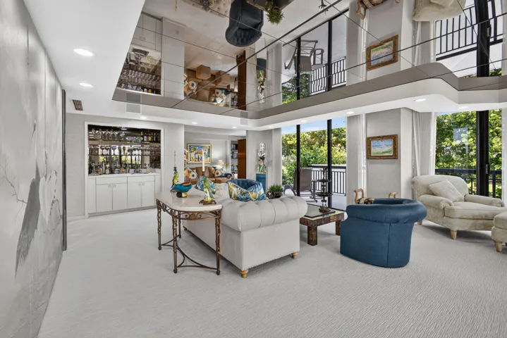 Spacious living area featuring a mirrored ceiling, built-in wet bar with cabinetry, full-height windows, and a second-story balcony overlooking the space
