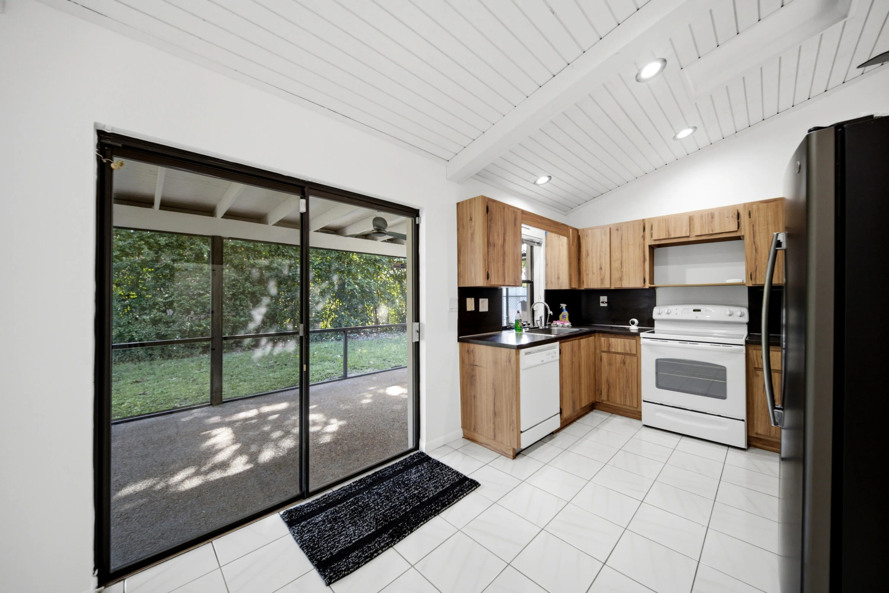Kitchen featuring wood cabinetry, black countertops, white tile flooring, and a white paneled vaulted ceiling with recessed lighting