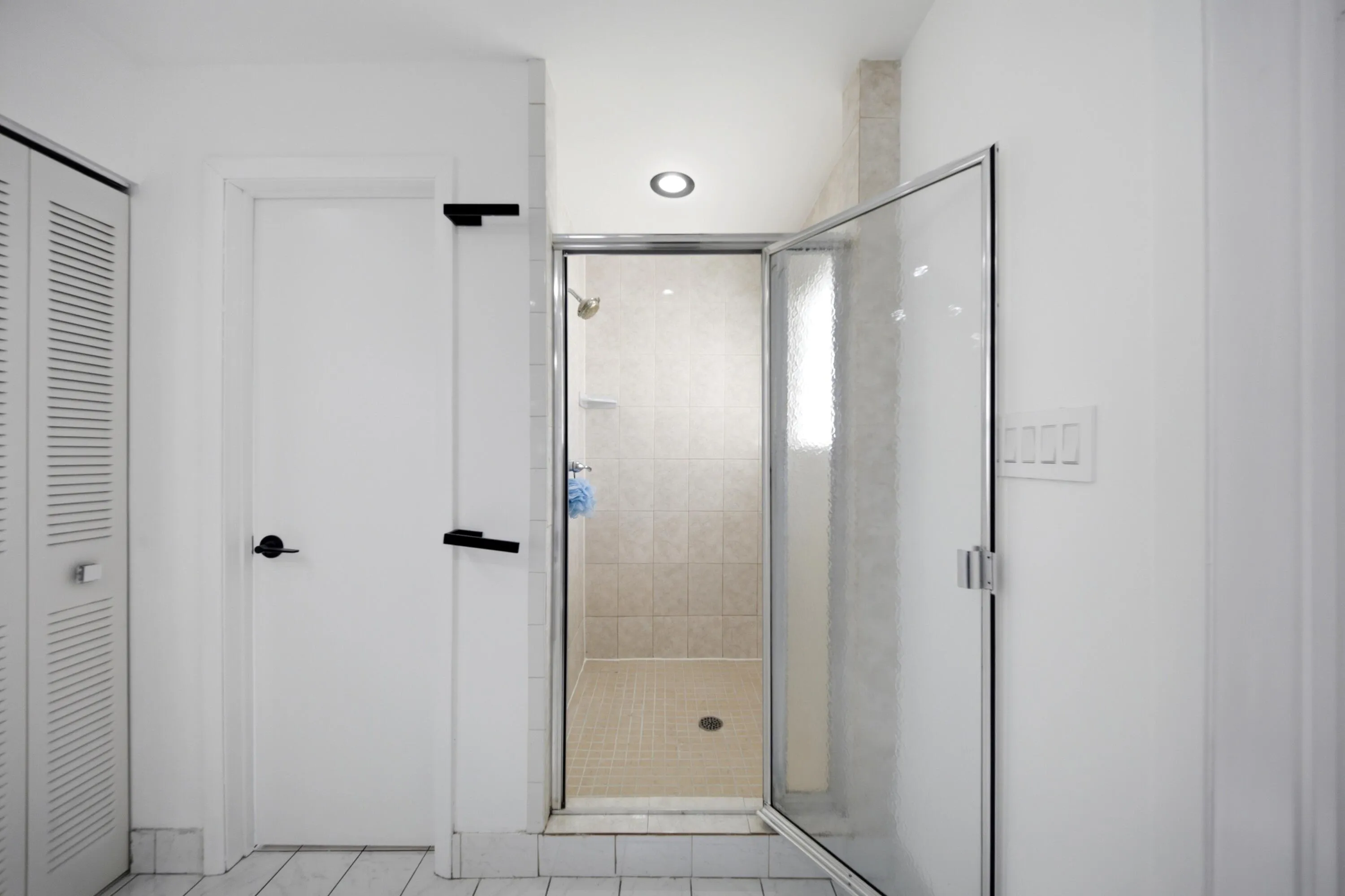 Walk-in shower featuring a tile surround, glass enclosure, and recessed lighting