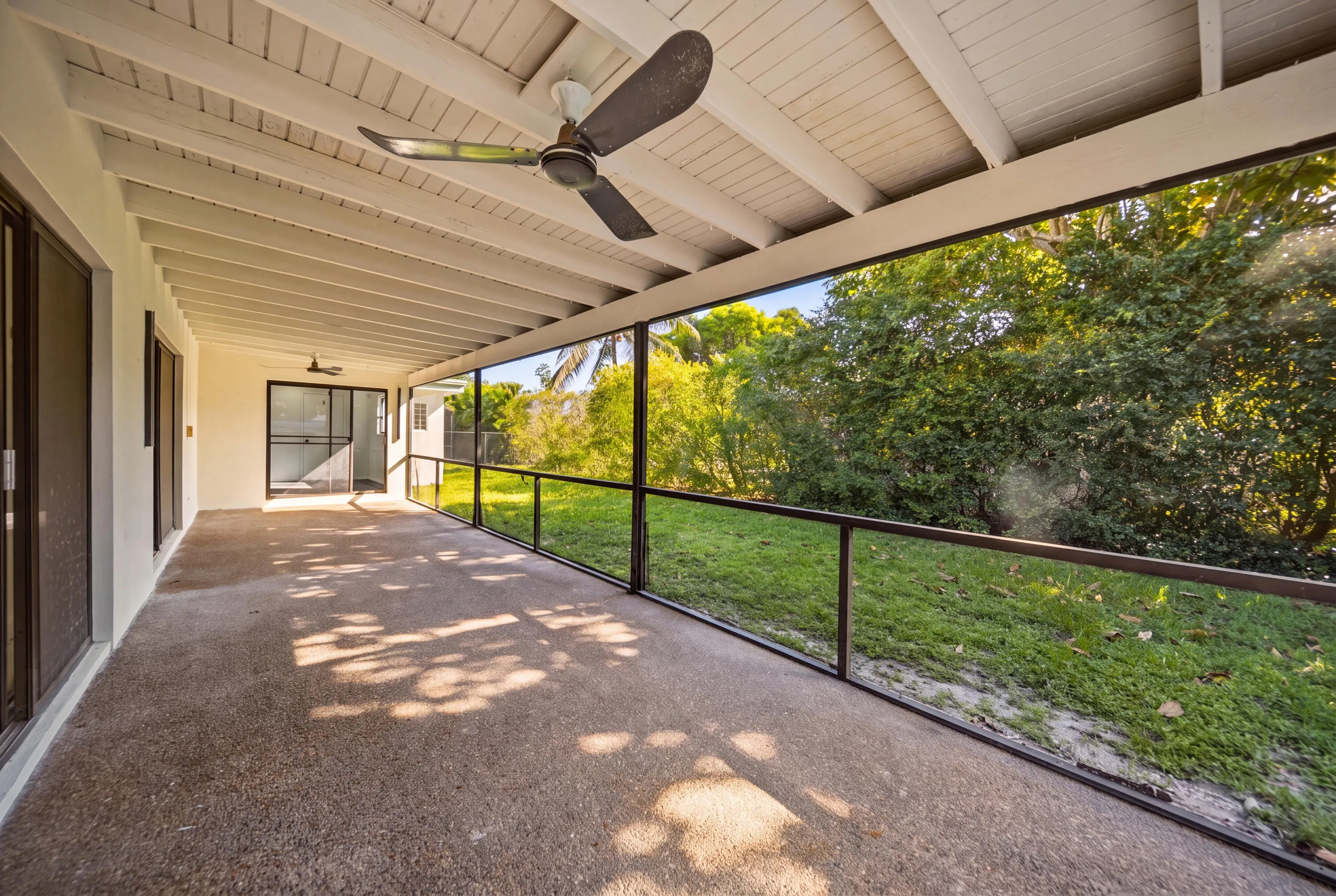 Expansive covered patio featuring exposed white ceiling beams, a ceiling fan, and a textured concrete surface