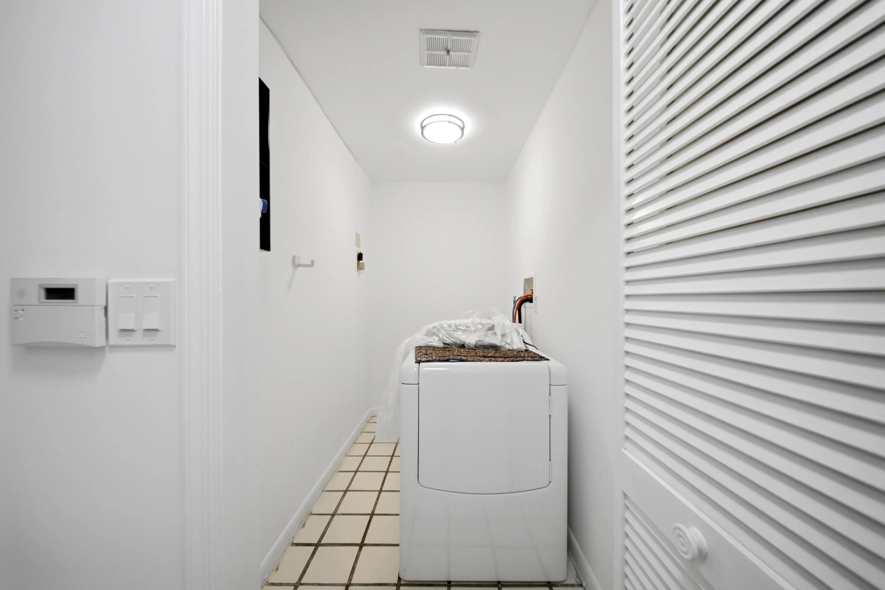 Dedicated laundry area featuring tile flooring, white walls, louvered bi-fold doors, and recessed ceiling lighting