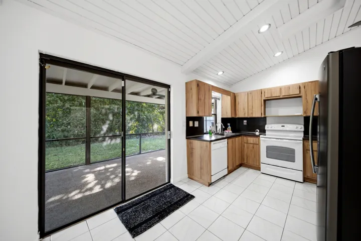 Kitchen featuring wood cabinetry, black countertops, white tile flooring, and a white paneled vaulted ceiling with recessed lighting