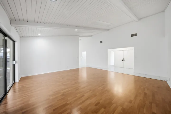 Spacious room featuring wood-finish flooring, white vaulted plank ceilings with exposed beams, recessed lighting, and large sliding glass doors